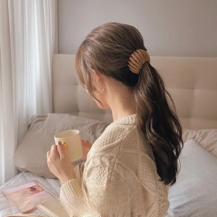 Twist-and-snap hair clip in tan shown holding a low ponytail from behind.