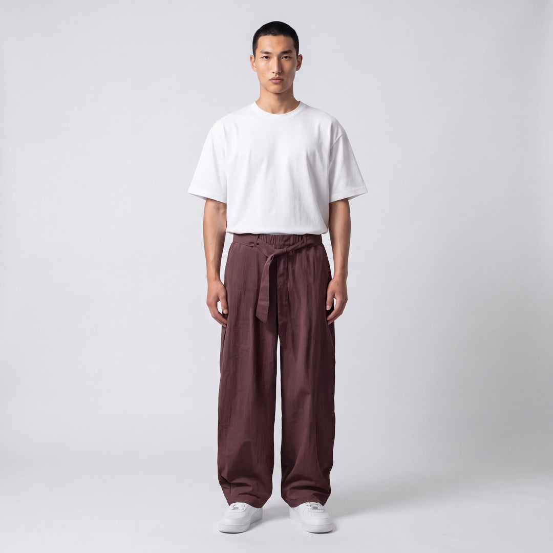 Full-length front view of a model in plum-brown wide-leg pants with a knotted waist tie and a white oversized tee. 7