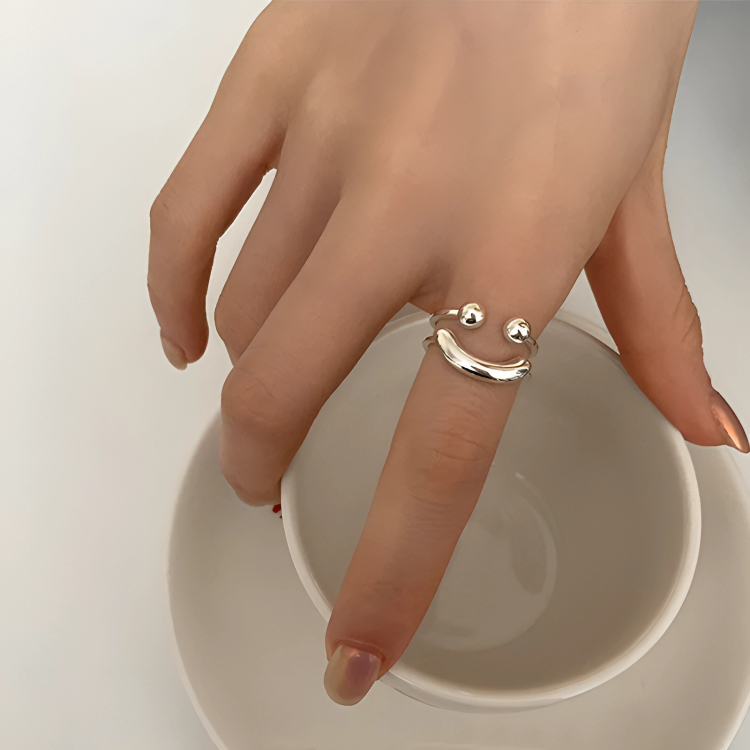 Smiley ring on a model's finger as her hand rests over the rim of a white cup, showing its curved smile. 2