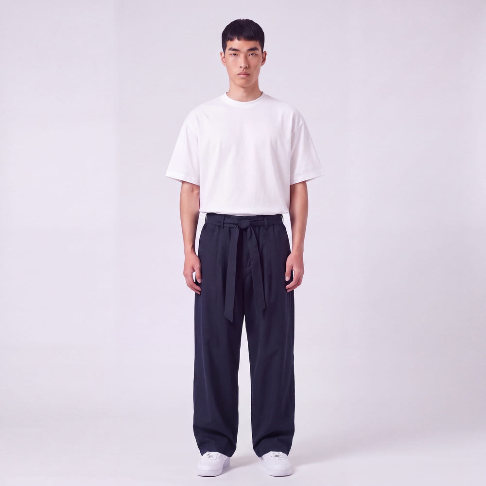 Full-length front view of a model wearing navy wide-leg pants with a fabric waist tie knotted at the front, with a white tee. 2