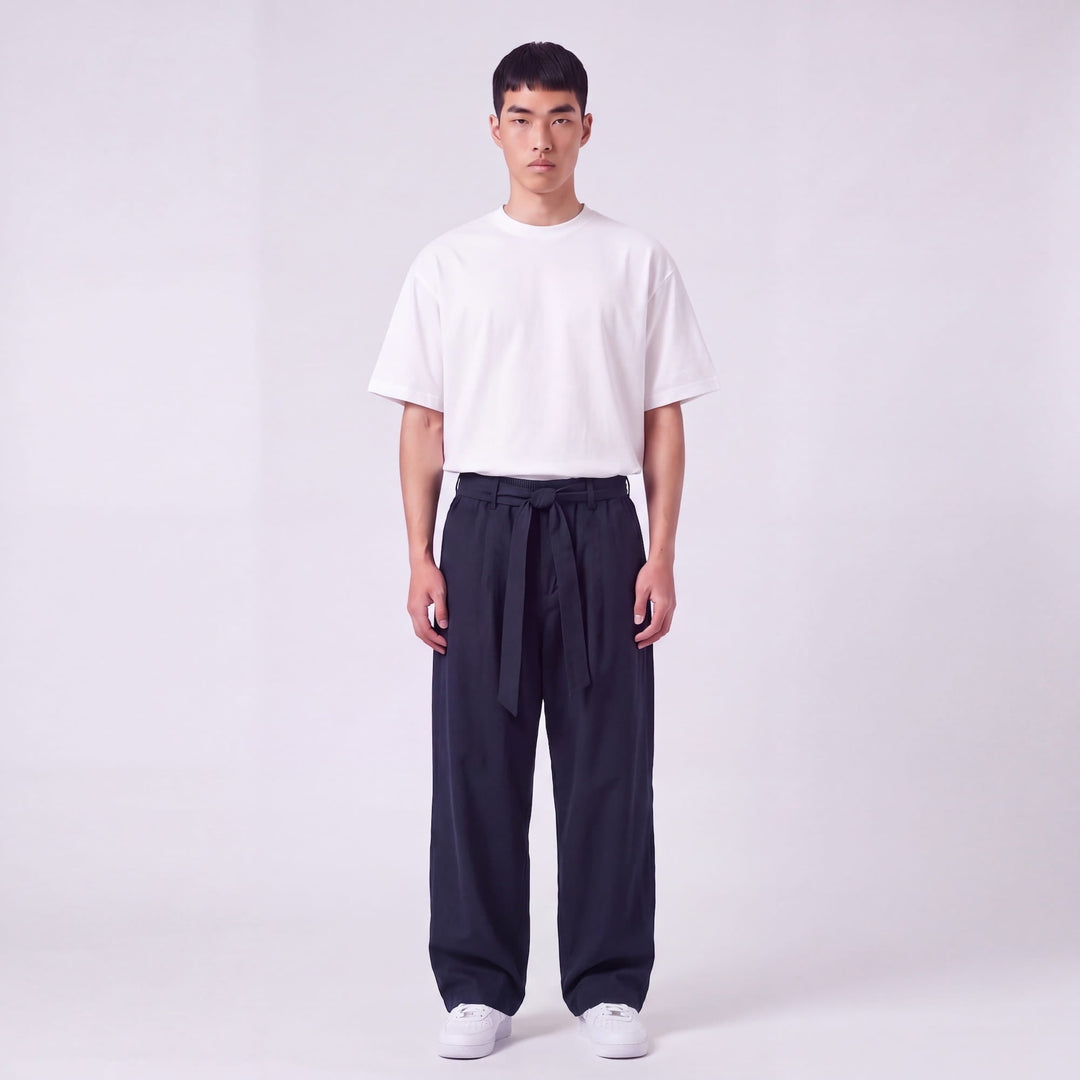Full-length front view of a model wearing navy wide-leg pants with a fabric waist tie knotted at the front, with a white tee. 2