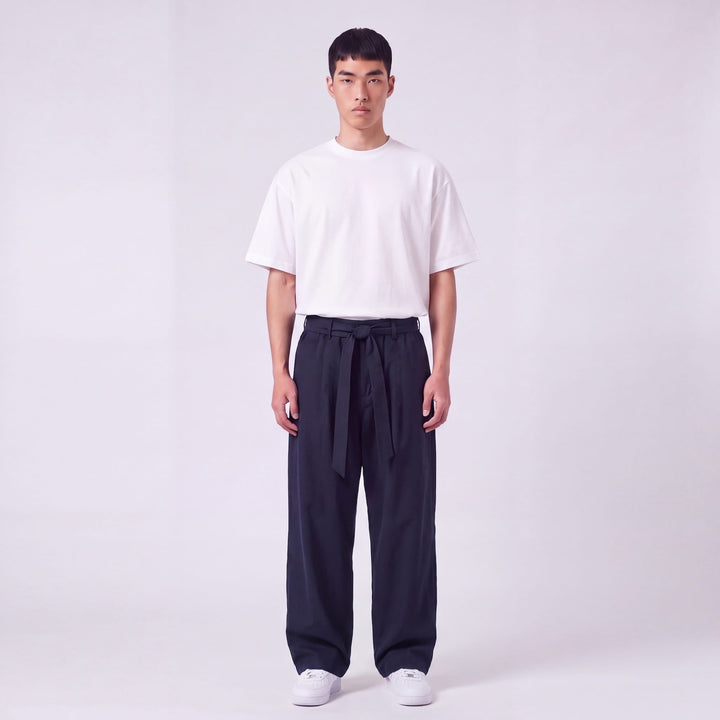 Full-length front view of a model wearing navy wide-leg pants with a fabric waist tie knotted at the front, with a white tee. 2