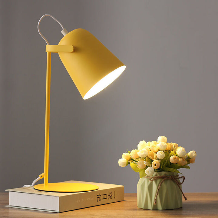 Yellow metal desk lamp glowing on a stack of books beside a small vase of cream roses 1