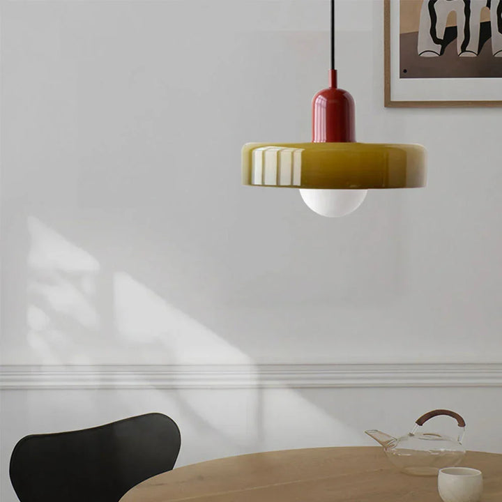 Olive glass shade with a red cap hanging above a round wooden table, black chair and glass teapot. 25