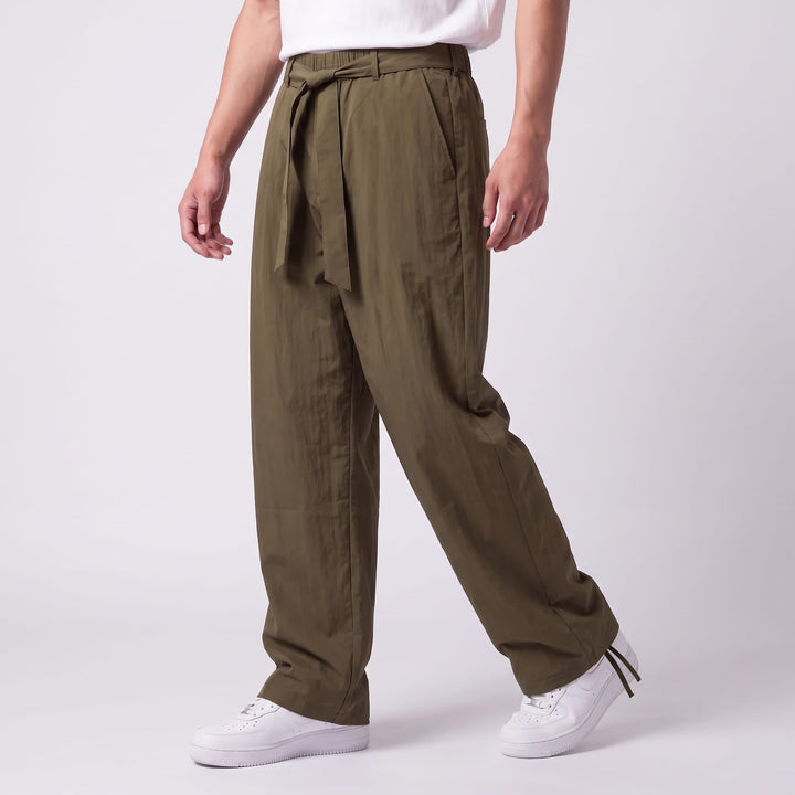 Three-quarter side view of a model walking in olive-green wide-leg pants with a knotted waist tie and ankle drawcords. 10