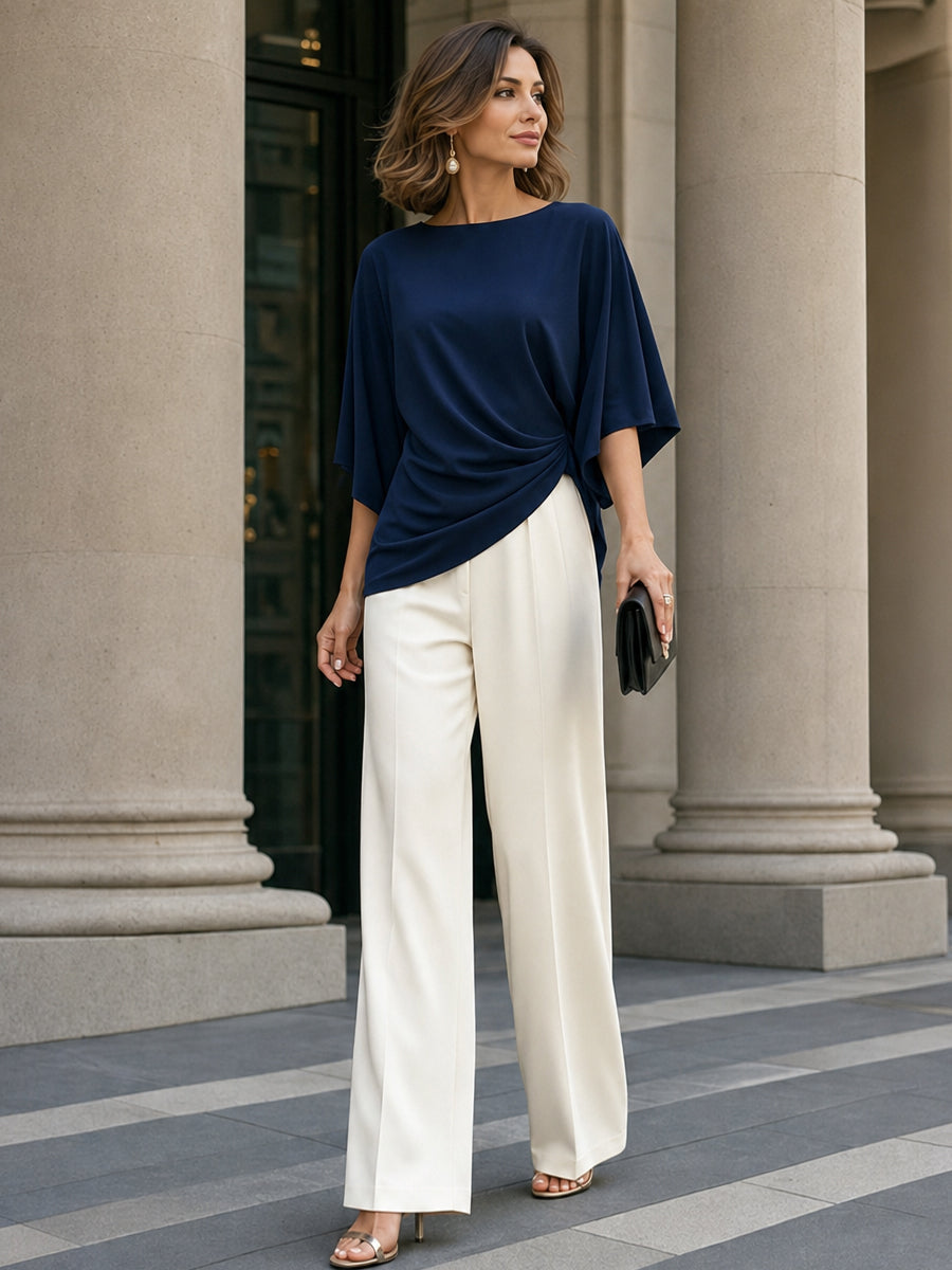 Model styling the navy draped blouse with cream pleated wide-leg trousers in front of large stone columns. 13