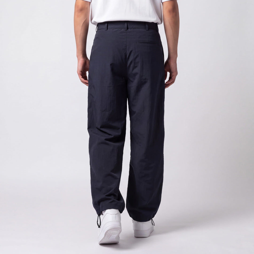 Back view of a model in navy pants showing the welt back pocket, belt loops, and cinched drawstring ankles over white sneakers. 6