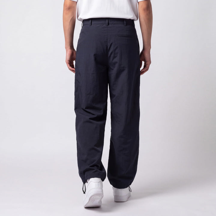 Back view of a model in navy pants showing the welt back pocket, belt loops, and cinched drawstring ankles over white sneakers. 6