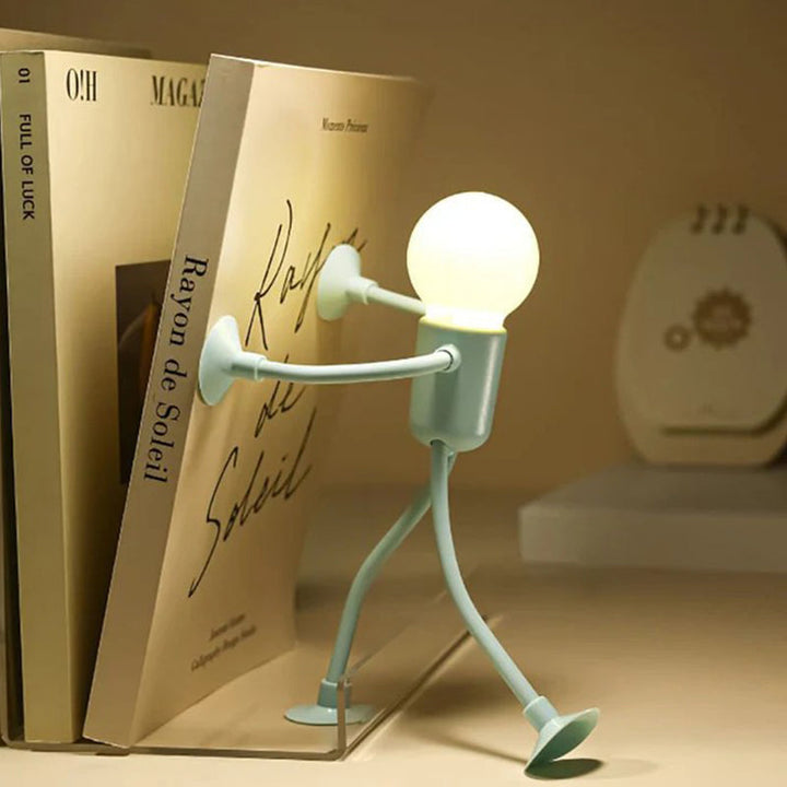 Mint green figure lamp pushing against a book on a shelf with its suction-cup hands.