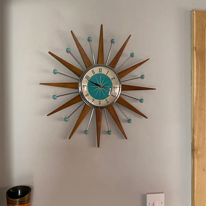 Starburst wall clock another view hung on a gray wall beside an oak door frame, a light switch and a vase.