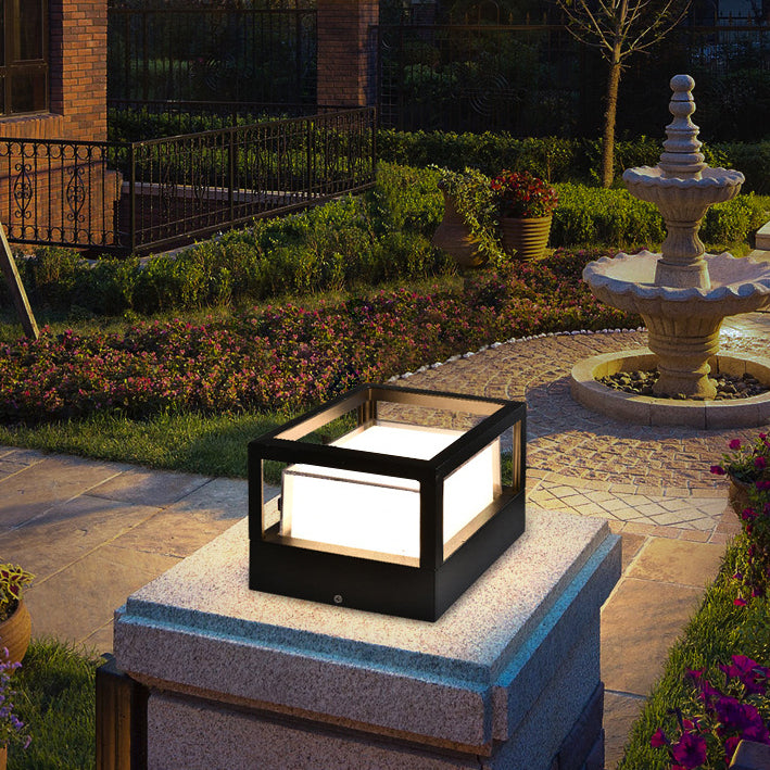 Square black cage-style lamp glowing on a granite gate pillar, set in a landscaped garden with a stone fountain. 2