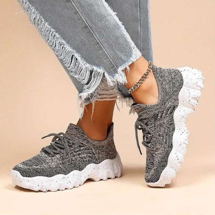 Model with legs crossed in gray marled knit sneakers, one foot angled to show the thick white speckled sole. 40