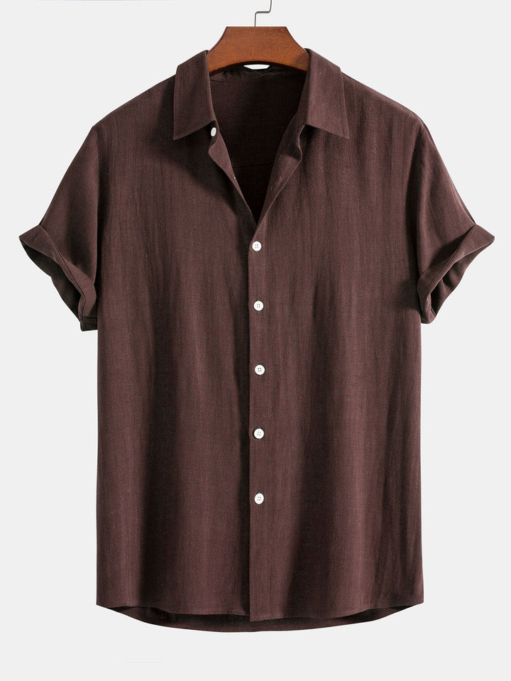 Dark chocolate brown short sleeve shirt on a wooden hanger, front view with white buttons and cuffed sleeves.