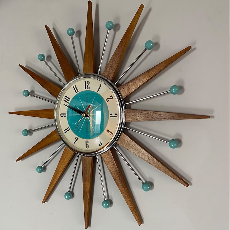 Starburst wall clock another view on a gray wall, with wooden rays, chrome rods and teal ball tips.