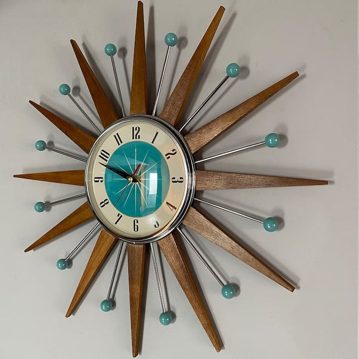 Starburst wall clock another view on a gray wall, with wooden rays, chrome rods and teal ball tips.