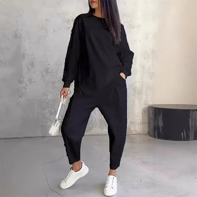 Woman wearing the black version of the sweatshirt and jogger pants, hand in pocket, with white sneakers and a white bag.