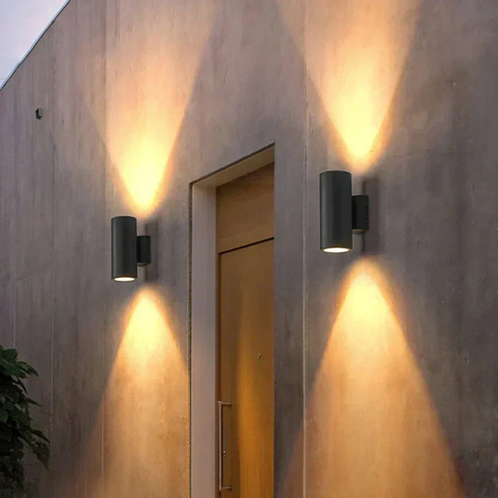 Black LED outdoor wall light, another view, flanking a wooden entry door on a concrete wall.