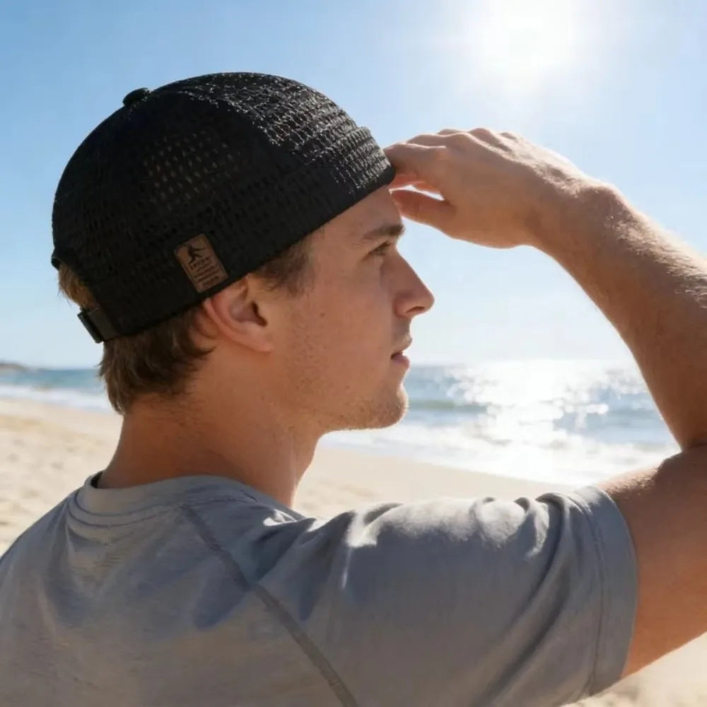 Man in a black mesh cap shading his eyes from the sun on a beach 10