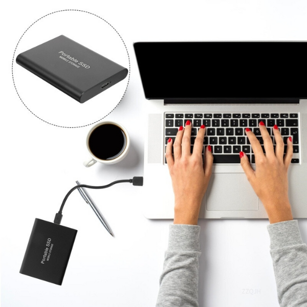 Black portable drive another view connected by cable beside a laptop and coffee cup.