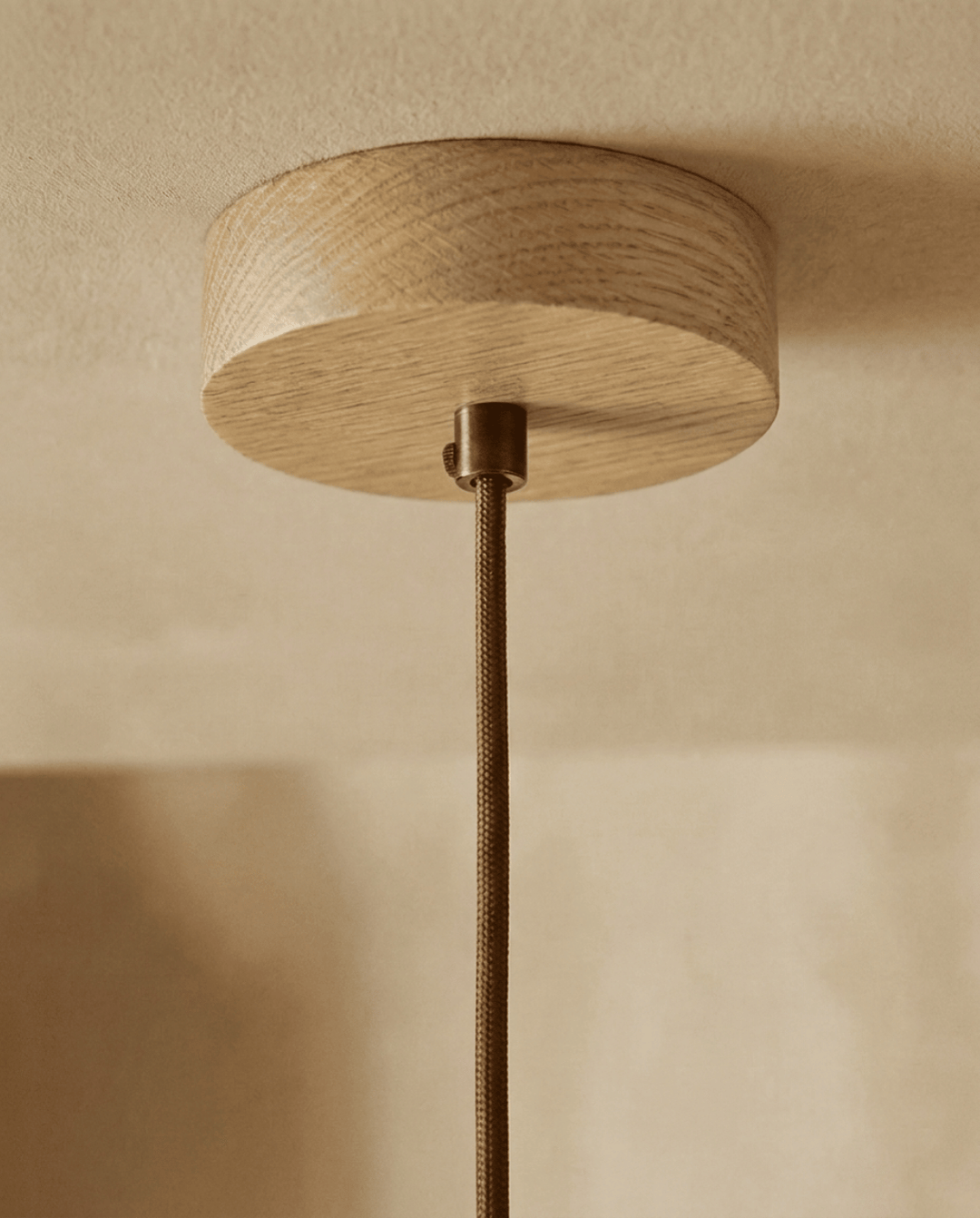 Travertine pendant light detail of the round light oak wood ceiling canopy and braided cord.