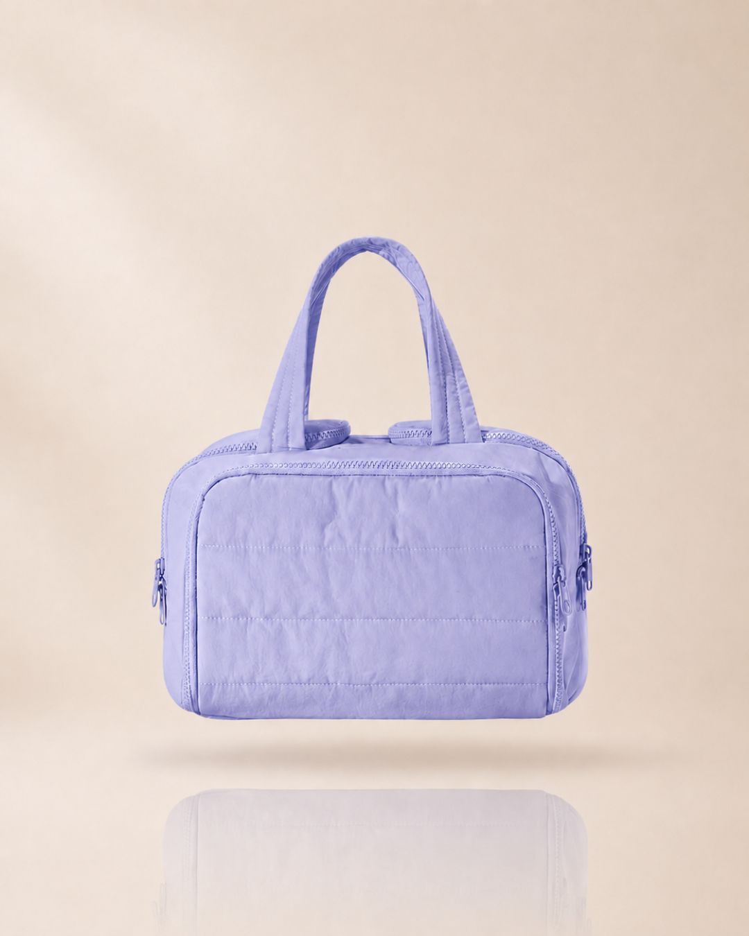 Lavender quilted bag with two handles, front view against a soft beige background.