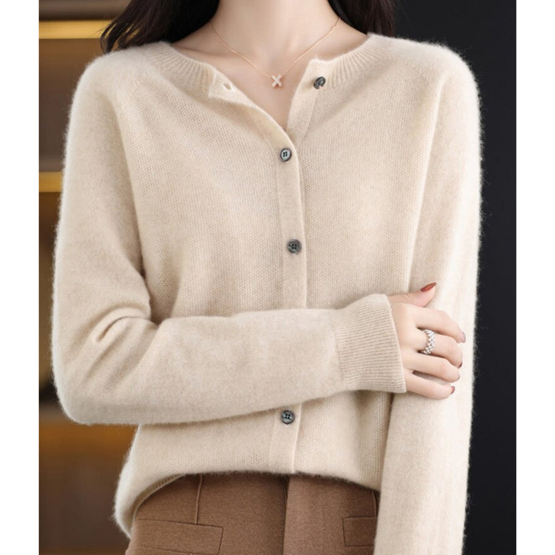 Woman wearing a cream beige fuzzy knit cardigan with ribbed cuffs and X pendant necklace, arm crossed, styled with camel trousers. 15