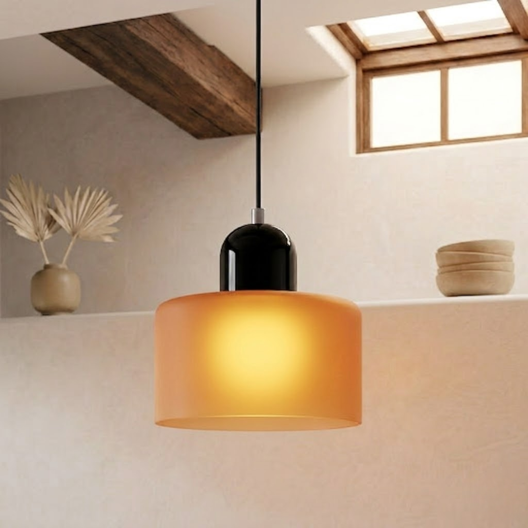 Illuminated frosted orange drum shade with a black glossy cap, casting a warm yellow glow in a minimalist interior. 16