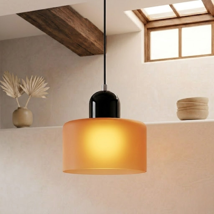 Illuminated frosted orange drum shade with a black glossy cap, casting a warm yellow glow in a minimalist interior. 16