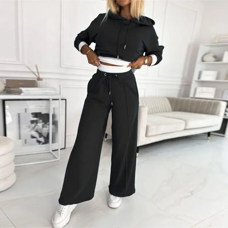 Model in a black hoodie and wide-leg pants, hands lifting the hem to reveal white inner trim 10