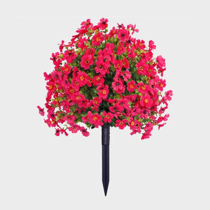 Hot pink artificial flower bush with green foliage on a black ground stake against a plain background.