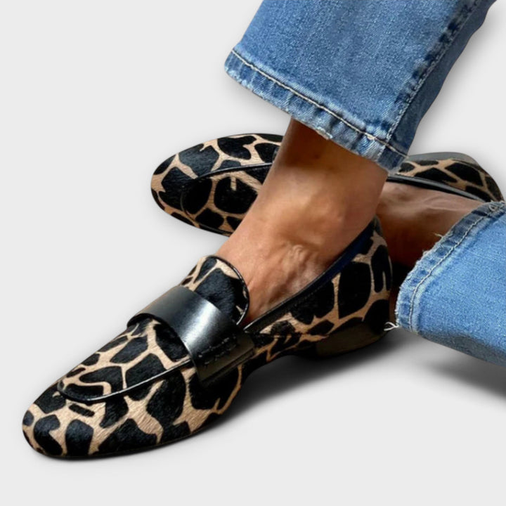 Closer, tighter view of the same loafer worn with cuffed jeans, showing the black strap and spotted tan and black fur-like upper. 2