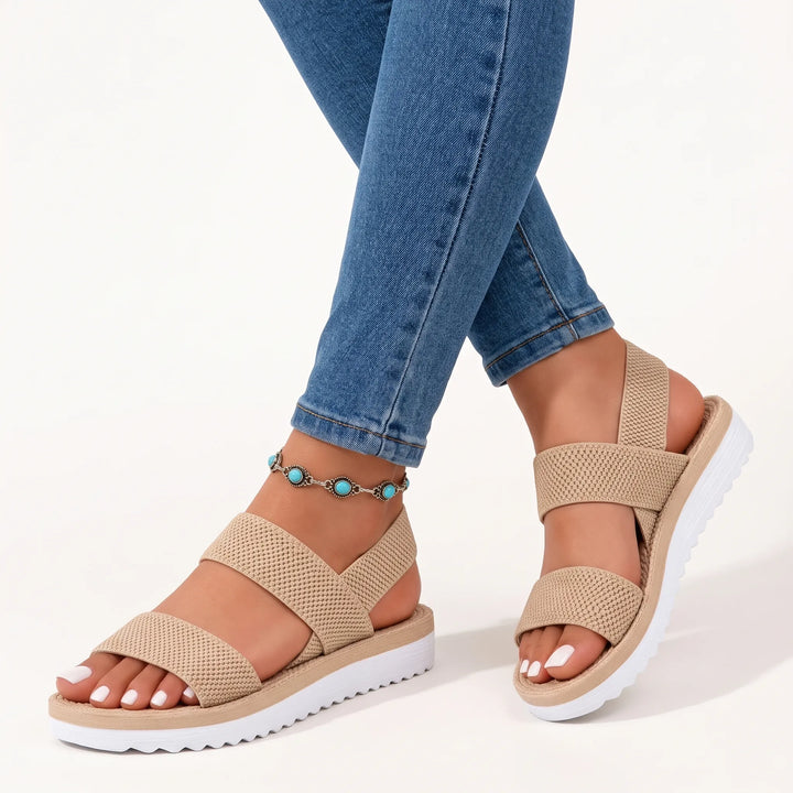 Beige knit-textured elastic sandals with white ridged soles, worn with blue skinny jeans and a turquoise anklet on a white 10