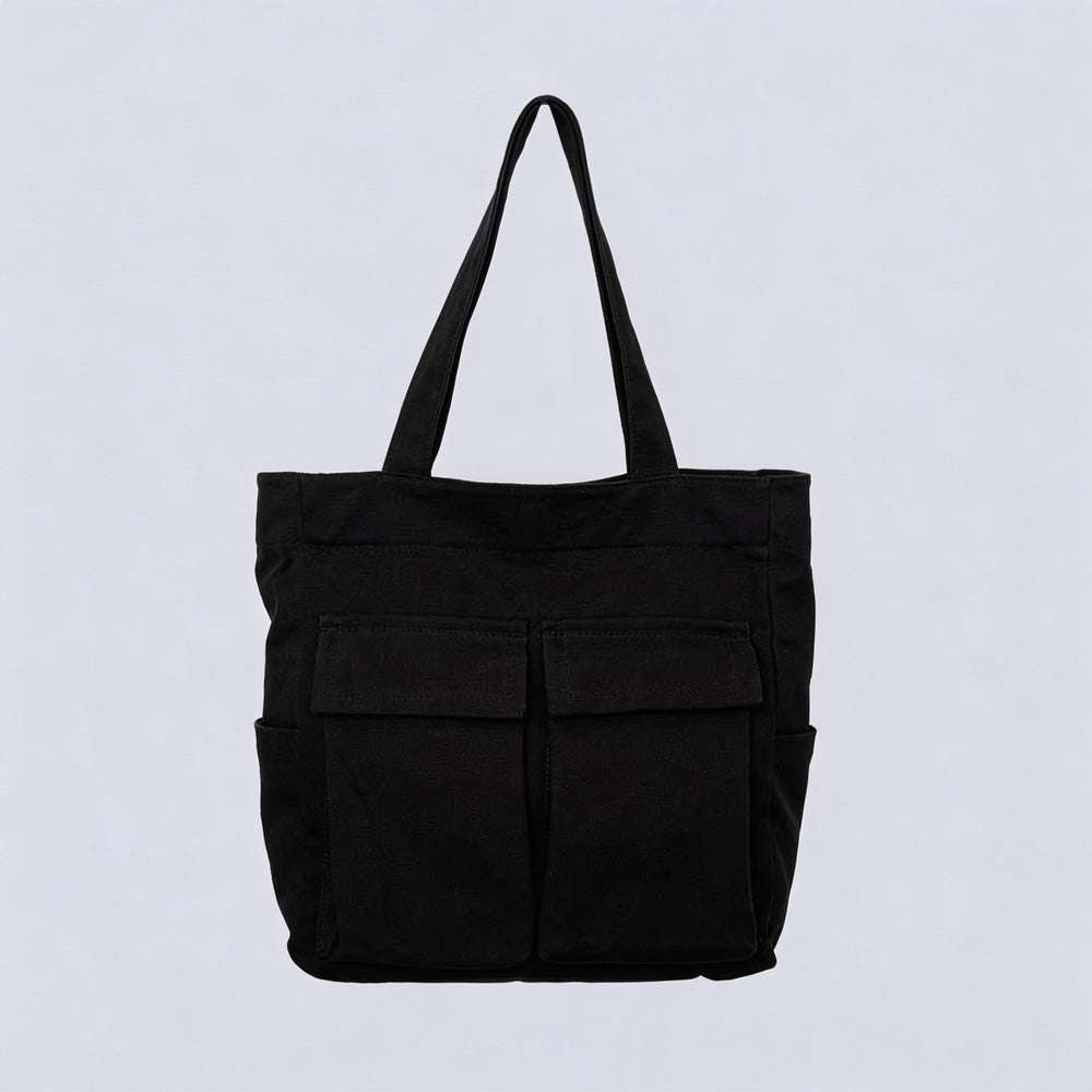 Black canvas tote bag with two front flap pockets, side pockets and a single shoulder handle, shown against a plain light background. 1