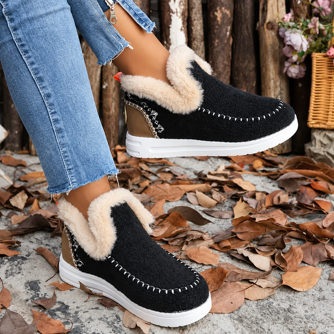 Side view of black fuzzy slip-on sneakers with cream plush collar, worn with cuffed jeans among fallen leaves 1