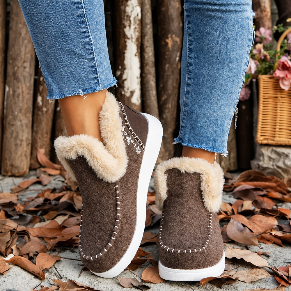 Rear three-quarter view of brown slip-ons with cream plush collar and snowflake embroidery, worn with frayed-hem jeans 2