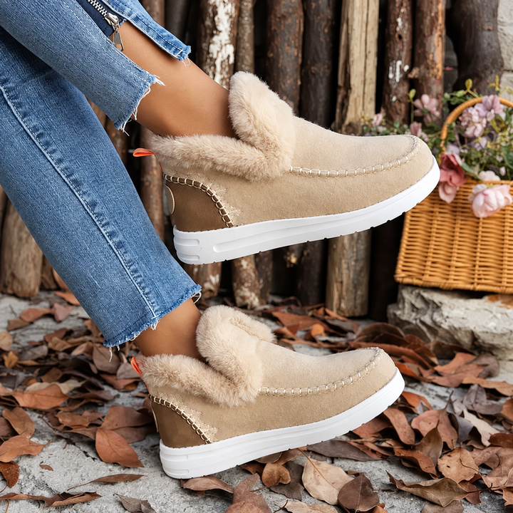 Beige suede-look slip-on sneakers with fluffy collar and white sole, worn beside a wicker basket of flowers 3