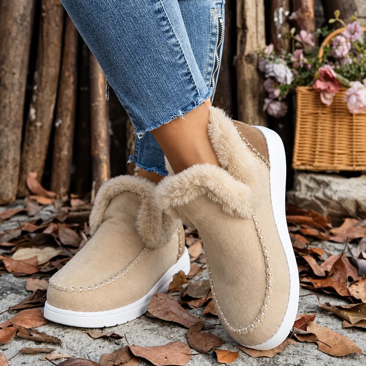 Front view of beige slip-on sneakers with plush trim worn with zippered jeans over fallen leaves 9