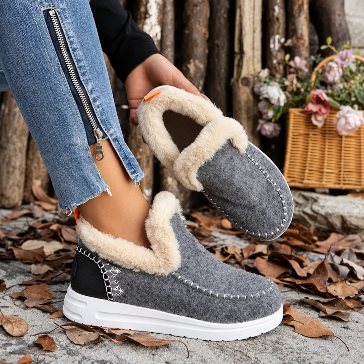 Gray slip-on sneakers with fuzzy collar, one worn and one held in hand to show the plush interior 5