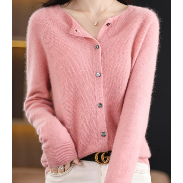 Woman wearing a soft pink fuzzy knit cardigan with gray buttons, one hand in the pocket of white pants, necklace visible. 2