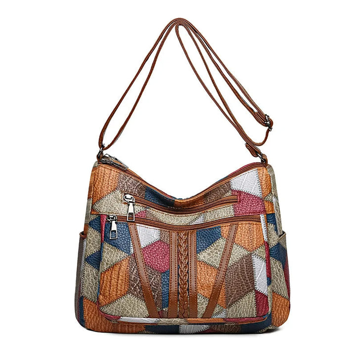 Front view of the patchwork bag on white with the strap raised overhead, showing two front zip pockets and braided brown trim. 9