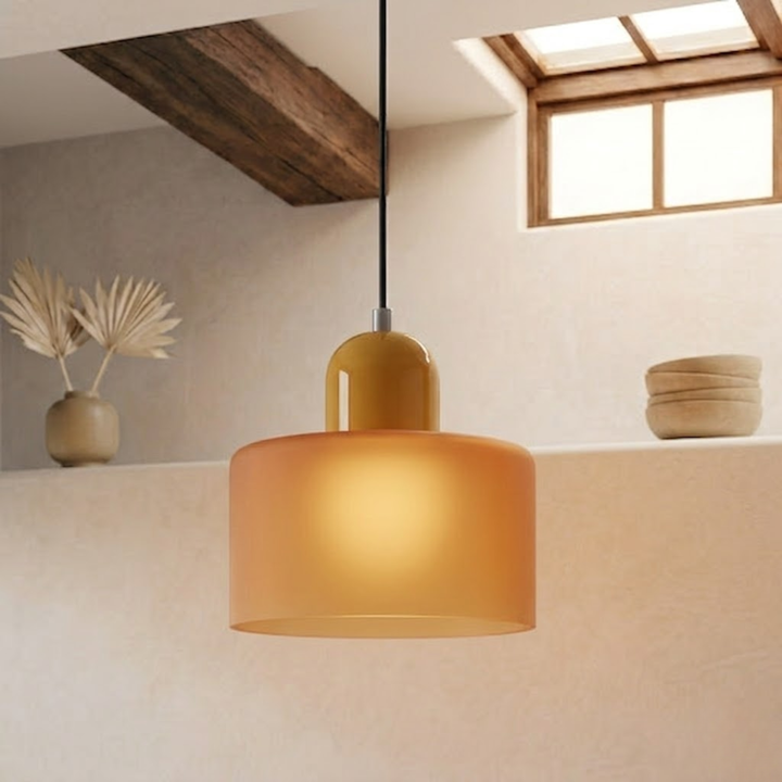 Softly lit frosted amber drum shade with a mustard-yellow cap, hanging on a black cord in a cream-walled room. 17