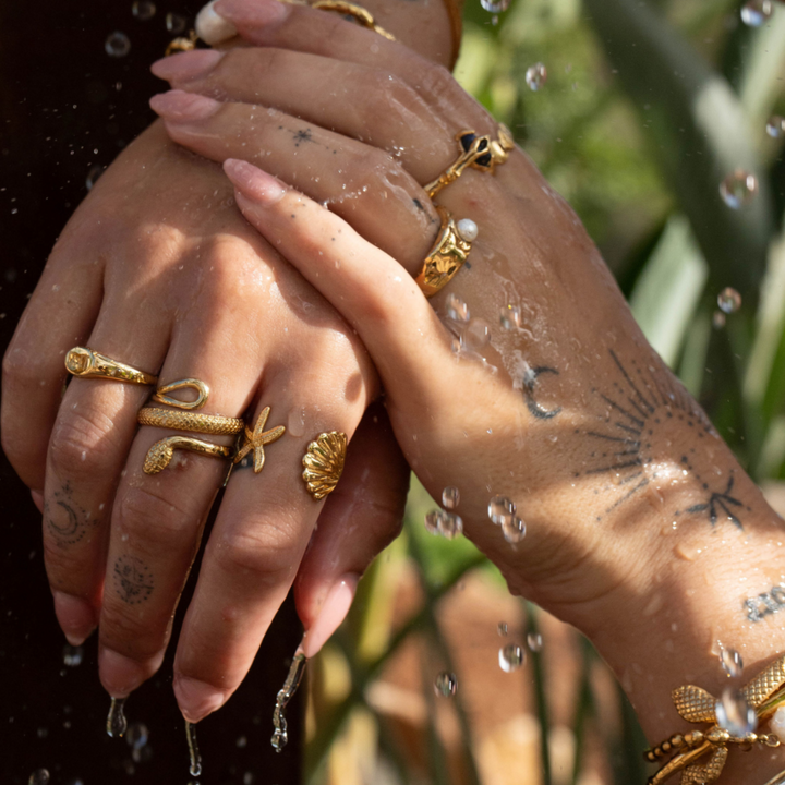 Wet hands with water droplets falling, wearing the gold snake ring stacked with a starfish ring, a shell ring and other gold rings. 6