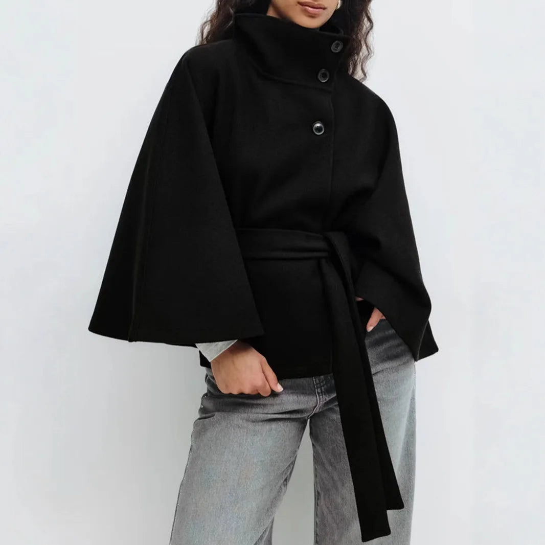 Black cape jacket with three buttons and long belt, worn with gray jeans, one hand in pocket 12