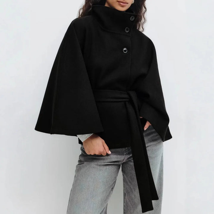 Black cape jacket with three buttons and long belt, worn with gray jeans, one hand in pocket 12
