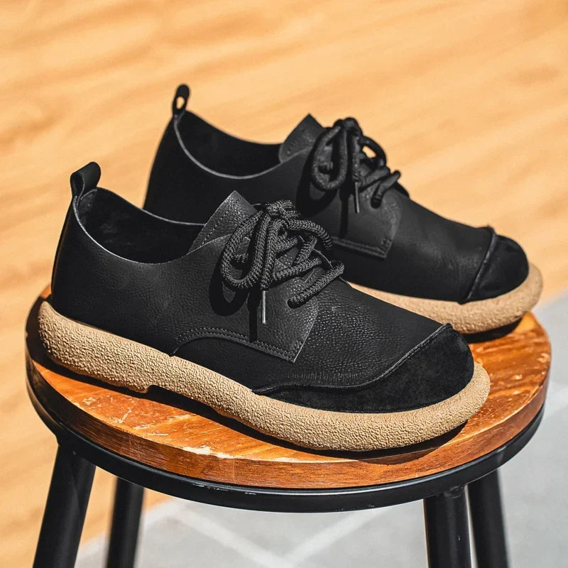 Black lace-up shoes with tan soles stacked on a round wooden stool 12