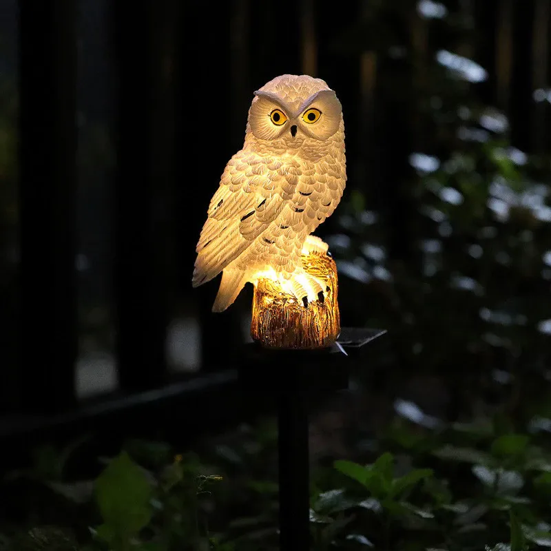 White owl light with yellow eyes glowing warmly against a dark fence and leaves 6