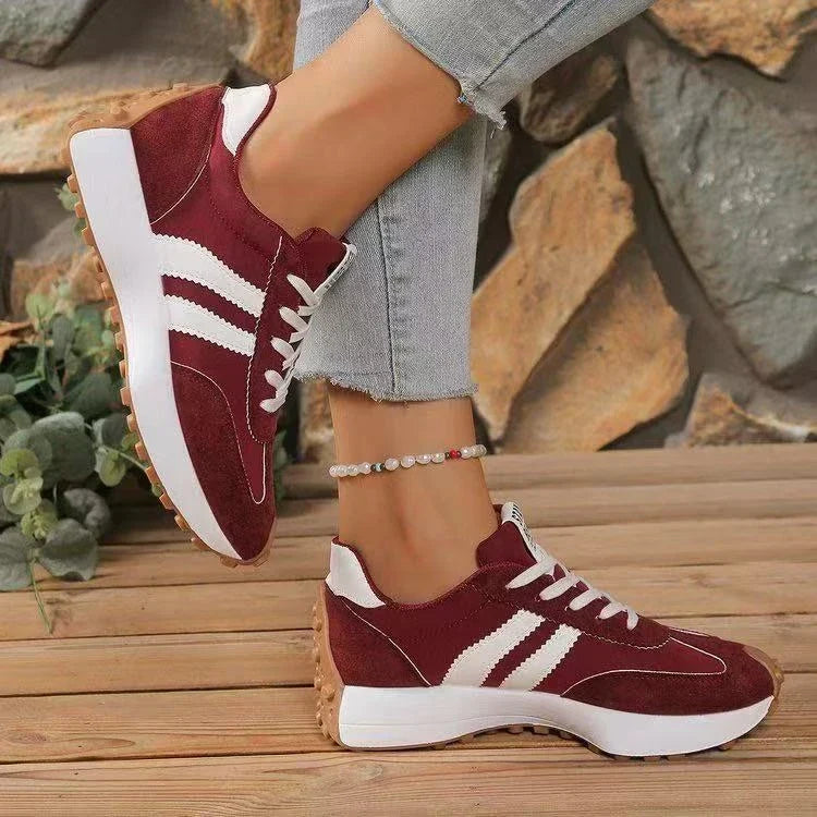 Burgundy trainers with white stripes worn with one foot lifted, showing the side profile and chunky sole 13