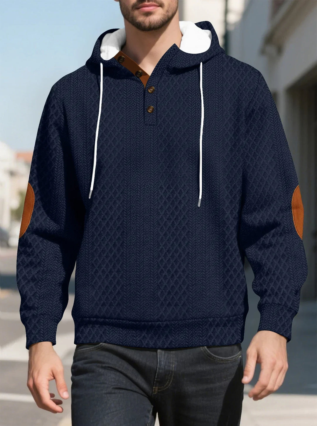 Front view of a man walking in a navy diamond-textured hoodie with brown elbow patches on a sunny street 13