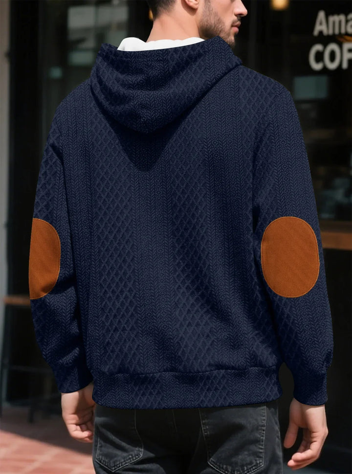 Back view of a man in a navy textured hoodie showing large brown elbow patches and ribbed hem 14