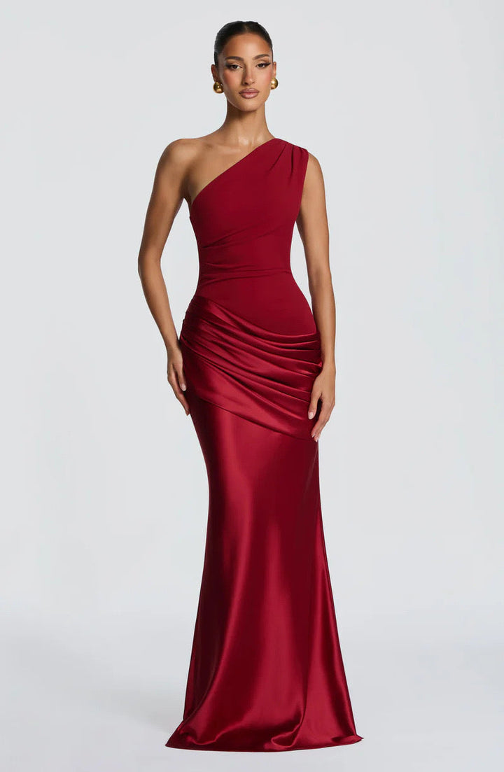 Model faces the camera in the burgundy red one-shoulder maxi dress, showing the fitted bodice, draped hip and flowing satin skirt. 21